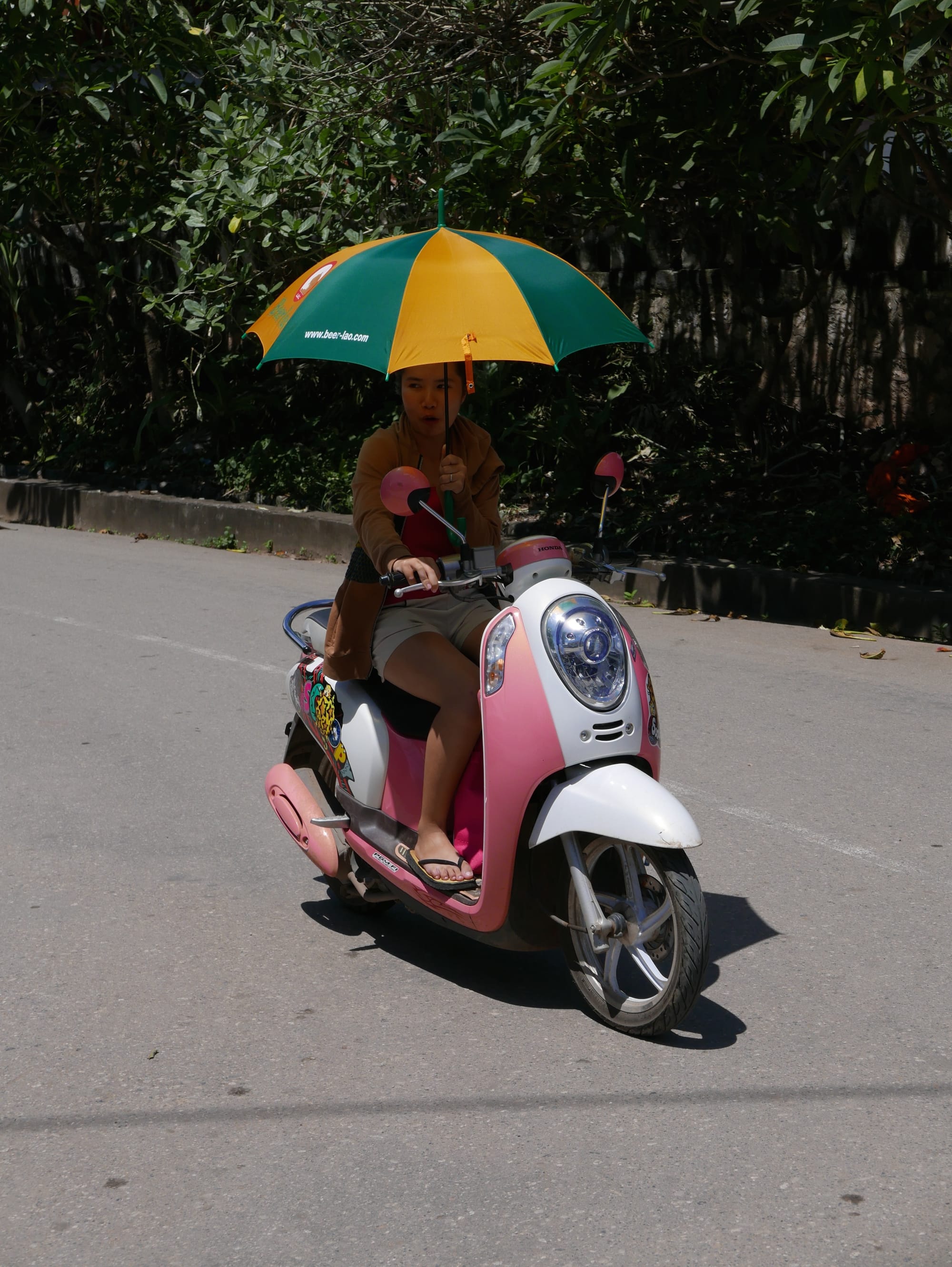 Photo by Author — motorbikes in Luang Prabang (ຫລວງພະບາງ/ຫຼວງພະບາງ), Laos — riding a motorbike one-handed with an umbrella