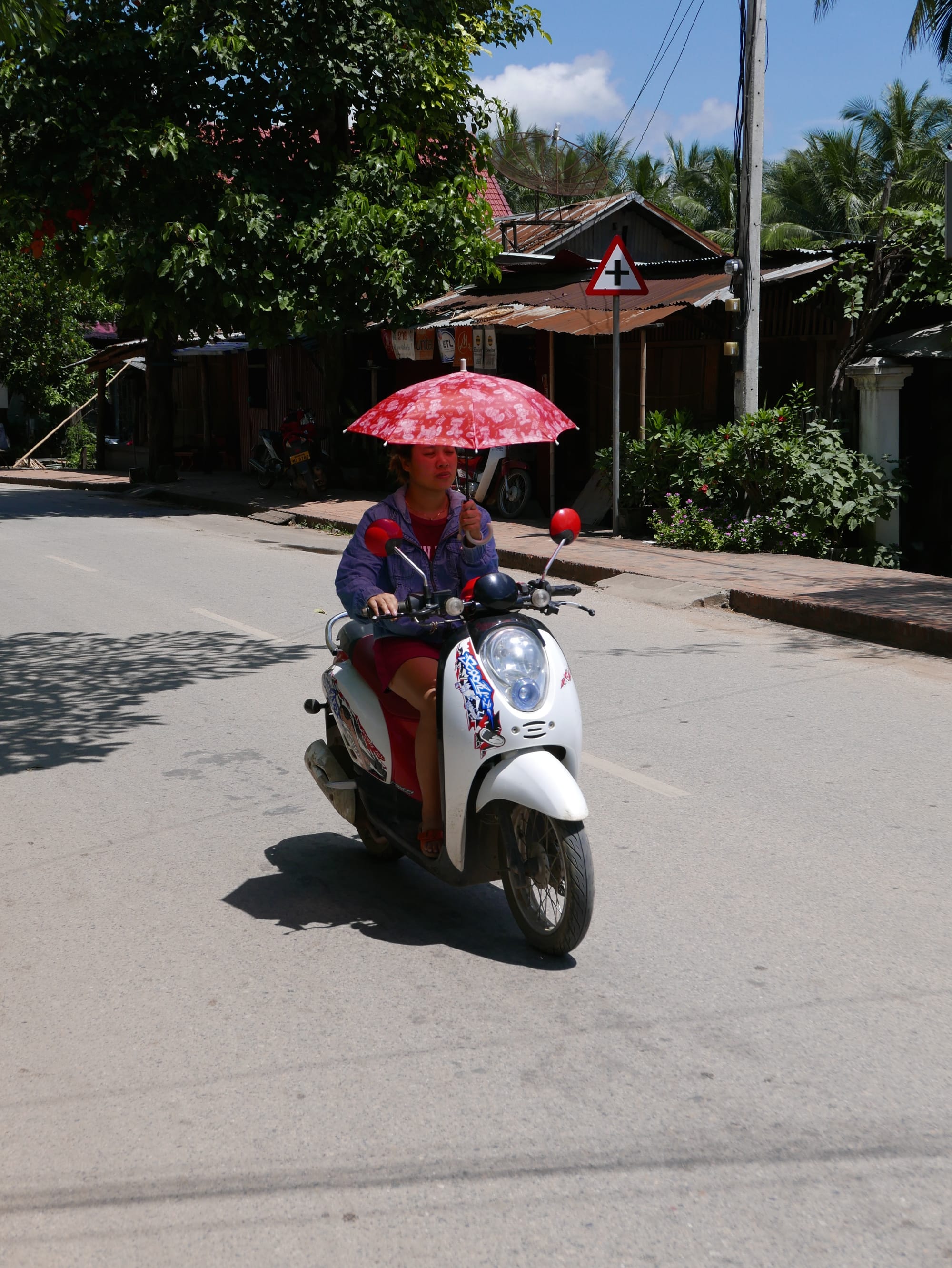 Photo by Author — motorbikes in Luang Prabang (ຫລວງພະບາງ/ຫຼວງພະບາງ), Laos — riding a motorbike with an umbrella — more one-handed skills