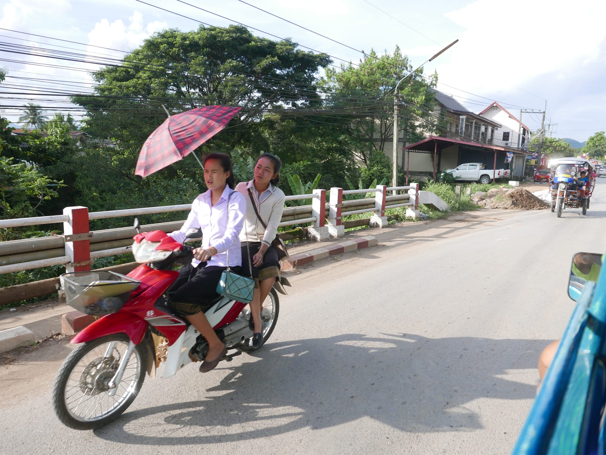 Photo by Author — motorbikes in Luang Prabang (ຫລວງພະບາງ/ຫຼວງພະບາງ), Laos — side-saddle with an umbrella — that takes skill