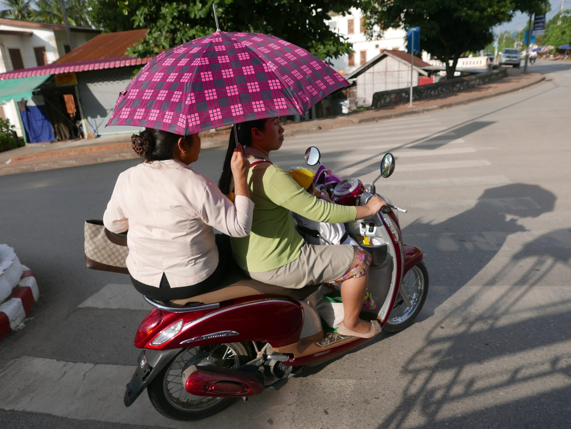 Photo by Author — motorbikes in Luang Prabang (ຫລວງພະບາງ/ຫຼວງພະບາງ), Laos — side-saddle with an umbrella — that takes skill